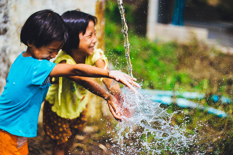 Two Pre-school aged children play in the water as it pours over them.